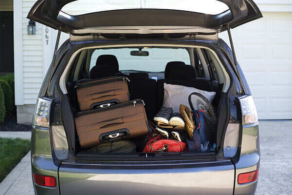 Trunk door of a mini van opened showing suitcases and travel gear