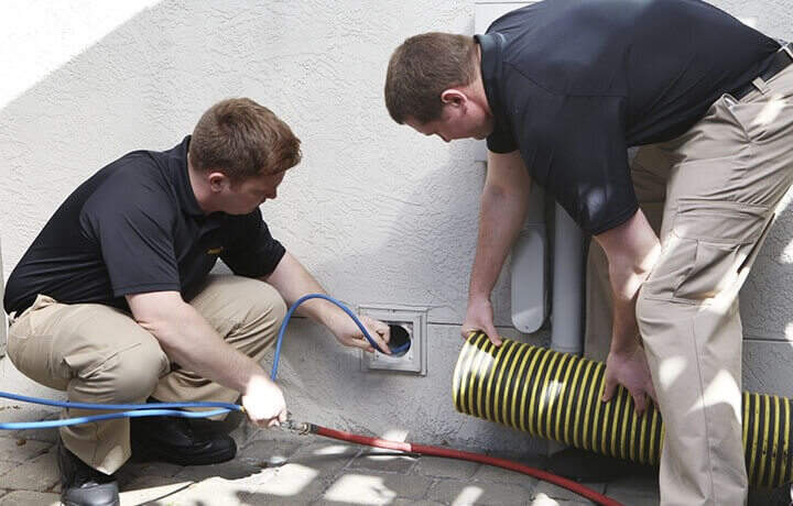 Stanley Steemer technicians inspecting a dryer vent opening on the exterior of a home.