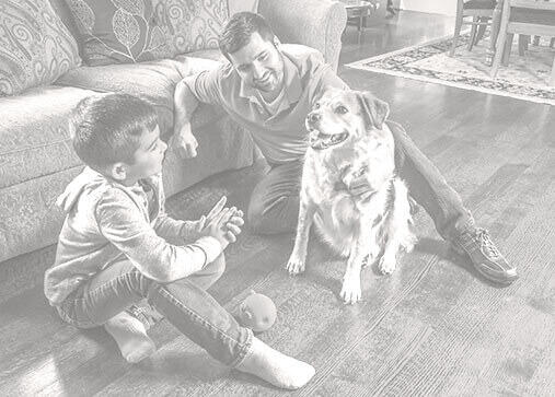 Father and son sitting on hardwood floors with their dog. 