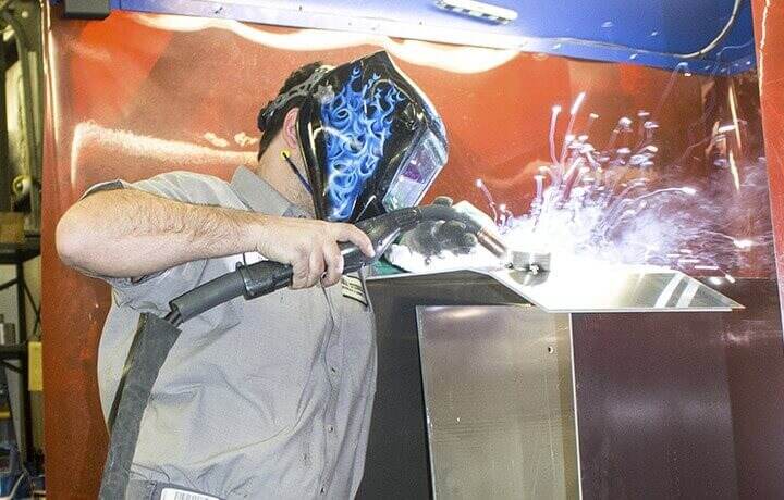 Metal smith worker with a face mask on and sparks flying.