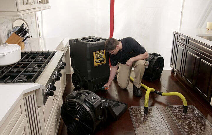 Stanley Steemer technician setting up water damage restoration equipment in kitchen.