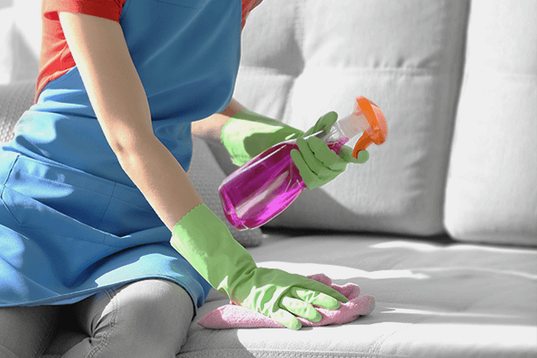 Woman with rubber gloves and apron on spot cleaning a couch